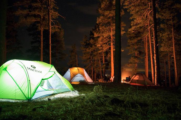 three dome tents with lights on forest beside campfire